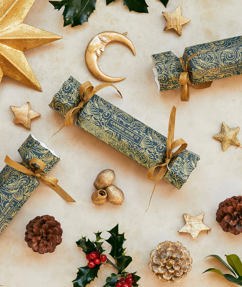 A selection of decorated Christmas crackers with gold and silver foil designs, matching with the six bottles of premium canned wines laid out on a festive background with holiday decorations.