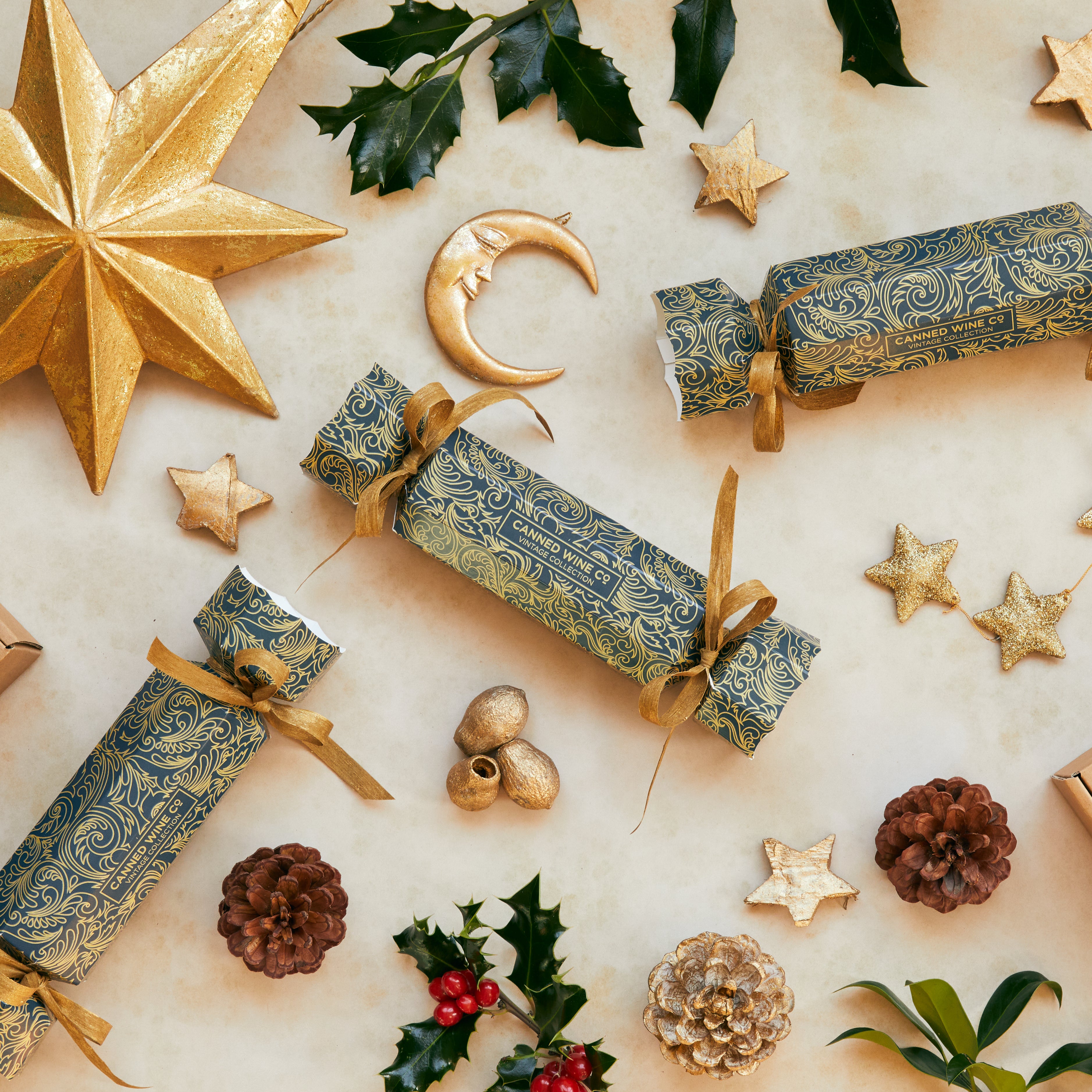 A selection of decorated Christmas crackers with gold and silver foil designs, matching with the six bottles of premium canned wines laid out on a festive background with holiday decorations.
